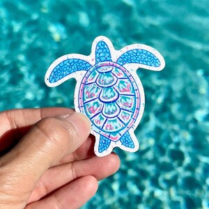 May include: A blue and pink glitter turtle sticker with a white background. The turtle is facing forward with its head and legs visible.