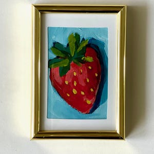 May include: A framed painting of a red strawberry with green leaves on a blue background.