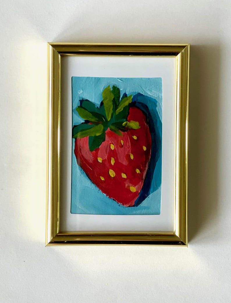 May include: A framed painting of a red strawberry with green leaves on a blue background.