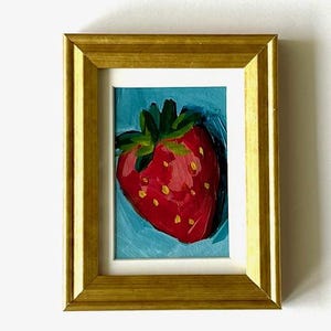May include: A framed painting of a red strawberry with green leaves on a blue background.