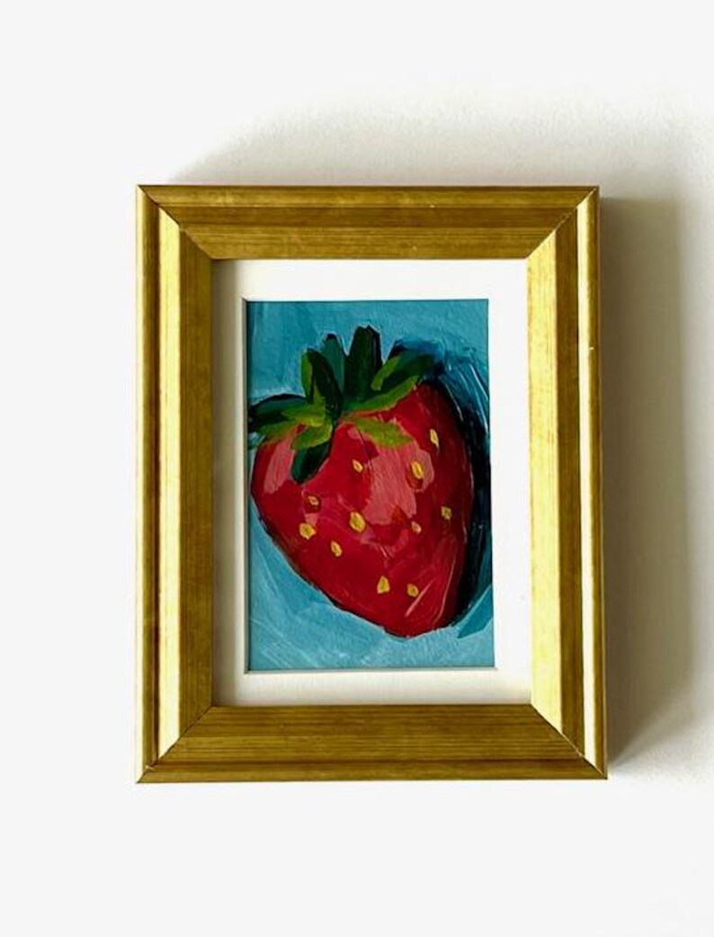 May include: A framed painting of a red strawberry with green leaves on a blue background.