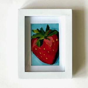 May include: A framed painting of a red strawberry with green leaves on a blue background.