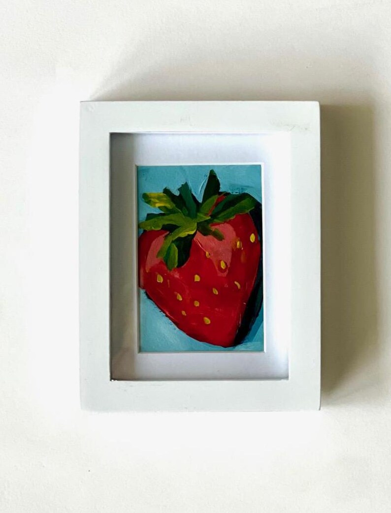 May include: A framed painting of a red strawberry with green leaves on a blue background.