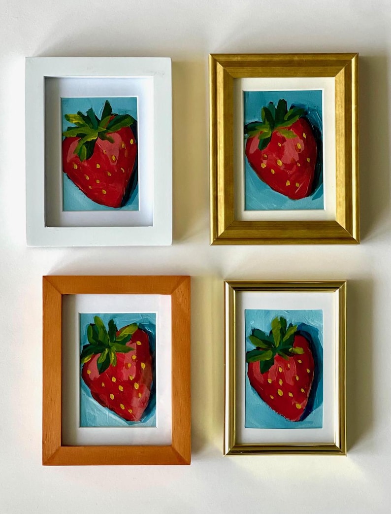 May include: Four framed paintings of red strawberries on a blue background. Each painting is in a different colored frame: white, gold, orange, and gold.