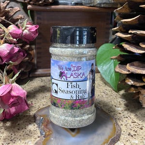 May include: A glass jar of fish seasoning and rub with a white label that says "We Are Dip Alaska" and "Fish, Seasoning & Rub".