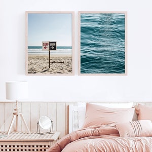 May include: Two framed prints of beach scenes. The first print shows a beach with a sign that reads "Surf Swim" with arrows pointing left and right. The second print shows a close-up of blue ocean waves.