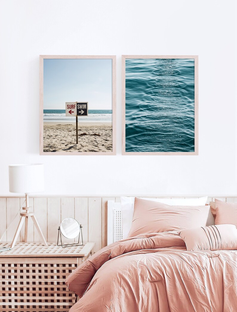May include: Two framed prints of beach scenes. The first print shows a beach with a sign that reads "Surf Swim" with arrows pointing left and right. The second print shows a close-up of blue ocean waves.