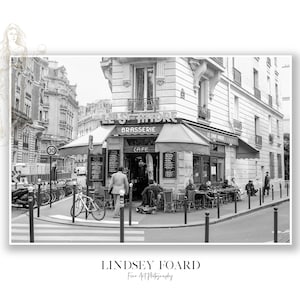May include: A black and white photograph of a Parisian cafe called "Le St Andre" with a sign that says "Brasserie" and "Cafe".  People are sitting outside the cafe at tables and chairs.  There are bicycles parked on the street.