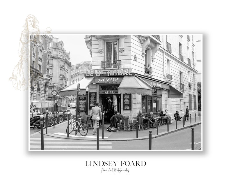 May include: A black and white photograph of a Parisian cafe called "Le St Andre" with a sign that says "Brasserie" and "Cafe".  People are sitting outside the cafe at tables and chairs.  There are bicycles parked on the street.
