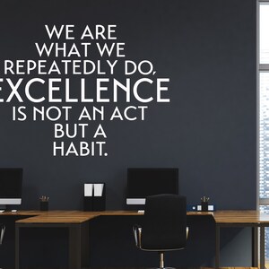 Peut inclure: Une citation motivante sur un mur gris fonc&eacute; dans un bureau moderne. La citation dit : "Nous sommes ce que nous faisons &agrave; r&eacute;p&eacute;tition. L'excellence n'est pas un acte mais une habitude."