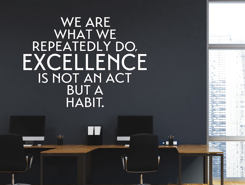 Peut inclure: Une citation motivante sur un mur gris fonc&eacute; dans un bureau moderne. La citation dit : "Nous sommes ce que nous faisons &agrave; r&eacute;p&eacute;tition. L'excellence n'est pas un acte mais une habitude."