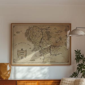 Può includere: Un soggiorno moderno di metà secolo con una credenza in legno, una poltrona beige e una mappa incorniciata della Terra di Mezzo. Un vaso geometrico dorato è posto sopra la credenza. Sono visibili anche una lampada da terra e una pianta.