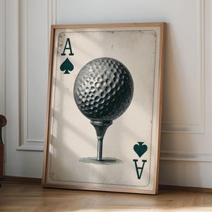 May include: A framed print depicting a golf ball on a tee, styled as the Ace of Spades playing card. The print has a vintage appearance with a light brown backdrop and a wooden frame. The golf ball is detailed with a textured surface.
