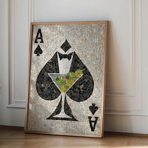May include: A framed mosaic artwork depicting the Ace of Spades card. The spade is black with a white tuxedo and a martini glass filled with olives. The artwork is in a wooden frame and leans against a white wall.