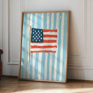 Puede incluir: Obra de arte enmarcada con una bandera estadounidense estilizada. La bandera tiene un campo azul con estrellas blancas y rayas rojas y blancas. El fondo tiene rayas verticales azules y blancas. La obra de arte está en un marco de madera.