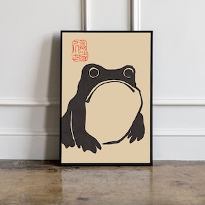 May include: A black and white illustration of a frog on a beige background. The frog is facing forward with its mouth closed. The image is framed in a black frame.