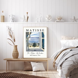 May include: A framed print of a painting by Henri Matisse titled "The Open Window". The painting depicts a view from a window overlooking a blue sea and a palm tree. The text "MATISSE" is printed in black at the top of the frame.