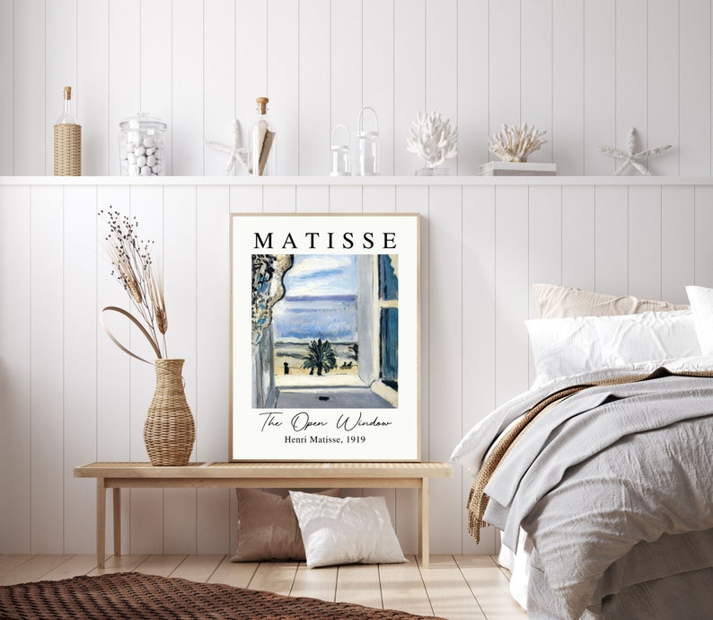 May include: A framed print of a painting by Henri Matisse titled "The Open Window". The painting depicts a view from a window overlooking a blue sea and a palm tree. The text "MATISSE" is printed in black at the top of the frame.
