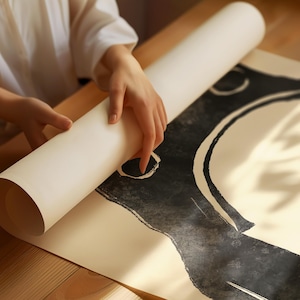 May include: A person unrolling a large sheet of paper with a black and white abstract design. The design features a large circle with a smaller circle inside, and a curved line extending from the circle.