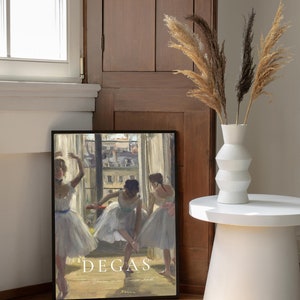 May include: A framed print of a painting by Edgar Degas titled "Three Dancers in an Exercise Hall". The painting depicts three ballerinas in white tutus practicing in a dance studio. The print is framed in black and has a white mat.