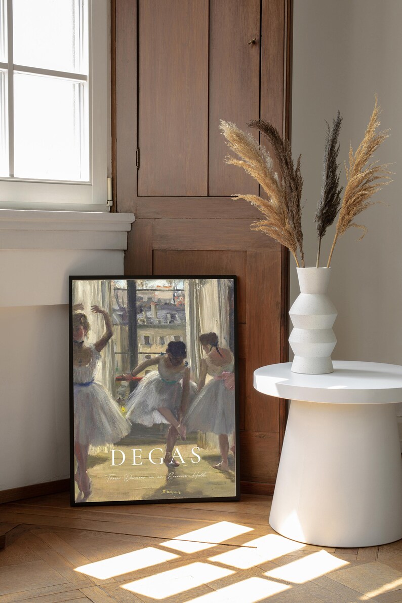 May include: A framed print of a painting by Edgar Degas titled "Three Dancers in an Exercise Hall". The painting depicts three ballerinas in white tutus practicing in a dance studio. The print is framed in black and has a white mat.