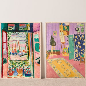 May include: Two framed paintings of abstract art. The painting on the left is a colorful scene with a window looking out onto a harbor with sailboats. The painting on the right is a room with a purple wall, a rug, and a sculpture.