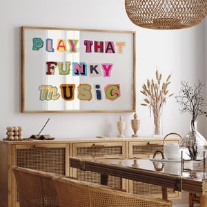 Puede incluir: Una impresi&oacute;n enmarcada con el texto "PLAY THAT FUNKY MUSIC" en letras de colores recortadas. La impresi&oacute;n est&aacute; colgada en una pared blanca sobre un armario de madera con puertas de rat&aacute;n tejido.