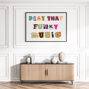 Puede incluir: Una impresi&oacute;n enmarcada con el texto "PLAY THAT FUNKY MUSIC" en letras de colores recortadas sobre un fondo blanco.
