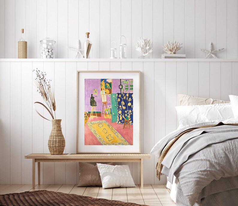 May include: A framed print of a painting depicting a room with a colorful rug, a green door, and a person painting on a canvas. The room is decorated with a blue and yellow patterned curtain.
