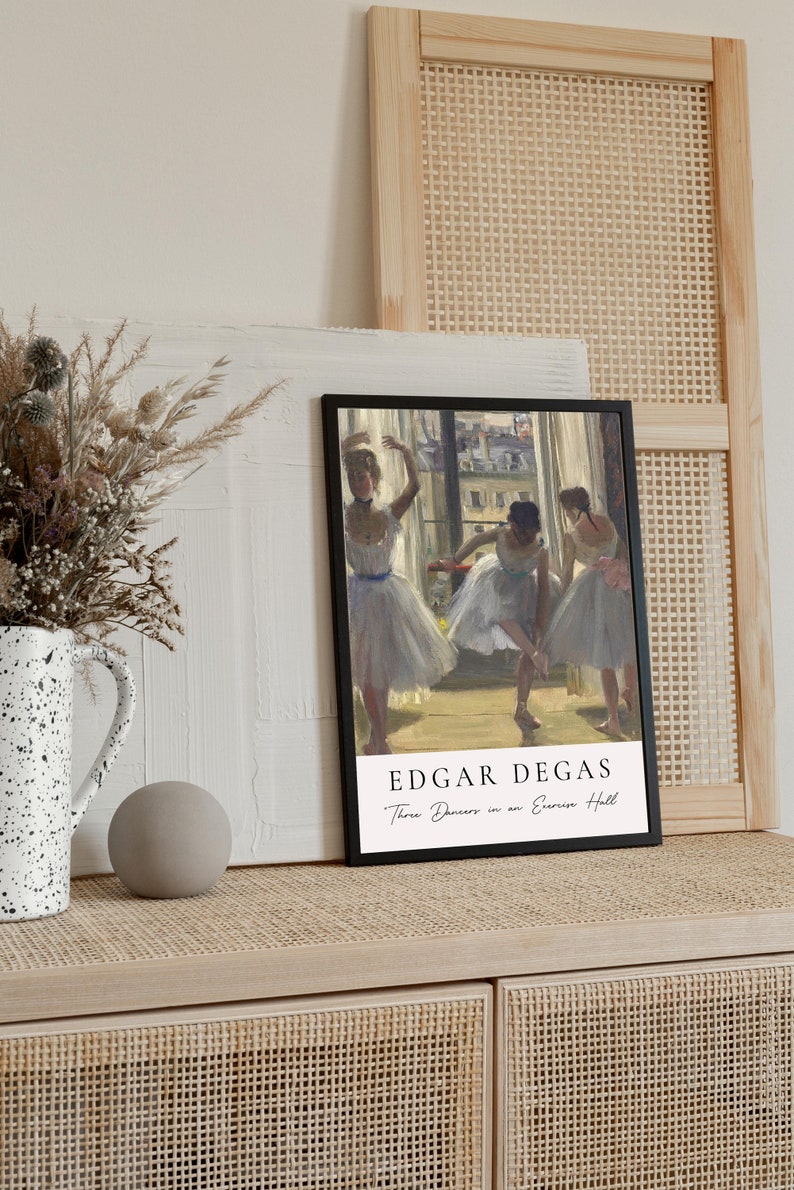 May include: A black framed print of a painting by Edgar Degas titled "Three Dancers in an Exercise Hall". The painting depicts three ballerinas in white tutus practicing in a dance studio.
