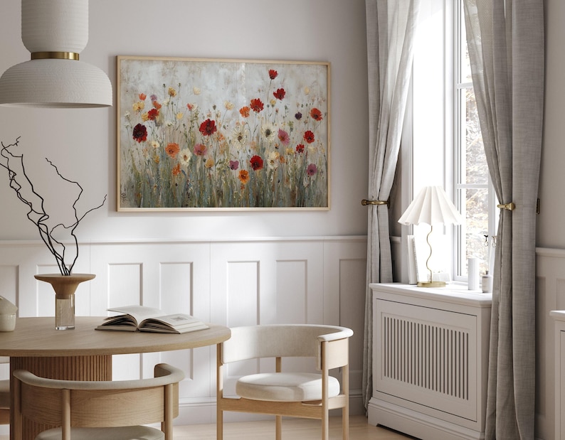 May include: A framed floral painting depicting a field of colourful flowers in shades of red, orange, and yellow. The artwork is displayed in a light-coloured room with a round wooden table, chairs, and a window with grey curtains.