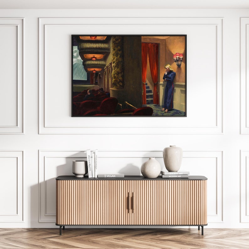 May include: A framed painting of a woman standing in a theater lobby. The woman is wearing a blue dress and is looking down. The theater lobby is decorated with red curtains and red velvet seats.