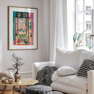 Puede incluir: Una pintura enmarcada de una ventana colorida con vista a un puerto. La pintura est&aacute; colgada en una pared blanca en una sala de estar con un sof&aacute; blanco, una mesa de caf&eacute; y una planta en maceta.