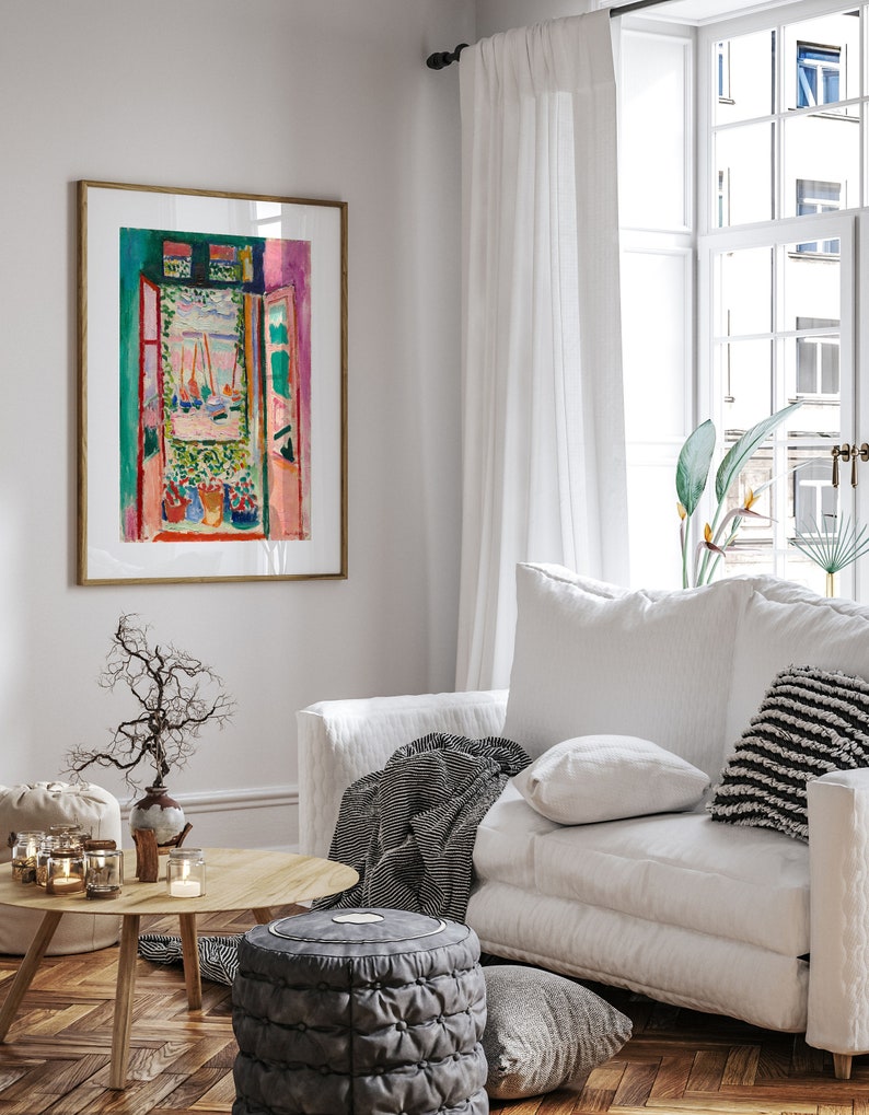 Puede incluir: Una pintura enmarcada de una ventana colorida con vista a un puerto. La pintura est&aacute; colgada en una pared blanca en una sala de estar con un sof&aacute; blanco, una mesa de caf&eacute; y una planta en maceta.