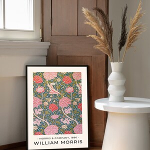 K&ouml;nnte beinhalten: Ein gerahmter Druck eines Blumenmusters mit rosa und wei&szlig;en Bl&uuml;ten auf dunkelgr&uuml;nem Hintergrund. Der Druck ist mit "William Morris" betitelt und enth&auml;lt den Text "Morris & Company, 1866".