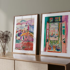May include: Two framed abstract paintings with colorful landscapes and a window view. The paintings are in wooden frames and are hanging on a wall.