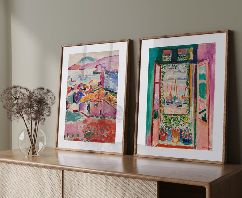 May include: Two framed abstract paintings with colorful landscapes and a window view. The paintings are in wooden frames and are hanging on a wall.