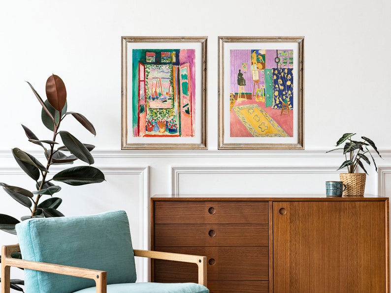 May include: Two framed art prints of paintings by Henri Matisse. The first print shows a view from a window with a pink wall and a green door. The second print shows a room with a purple wall, a yellow rug, and an easel with a painting on it.