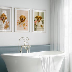 May include: Three framed prints featuring a golden retriever in a bathroom setting. One print shows the dog brushing its teeth, another in a bubble bath with rubber ducks, and the third with a hairdryer. The prints are displayed above a white bathtub.
