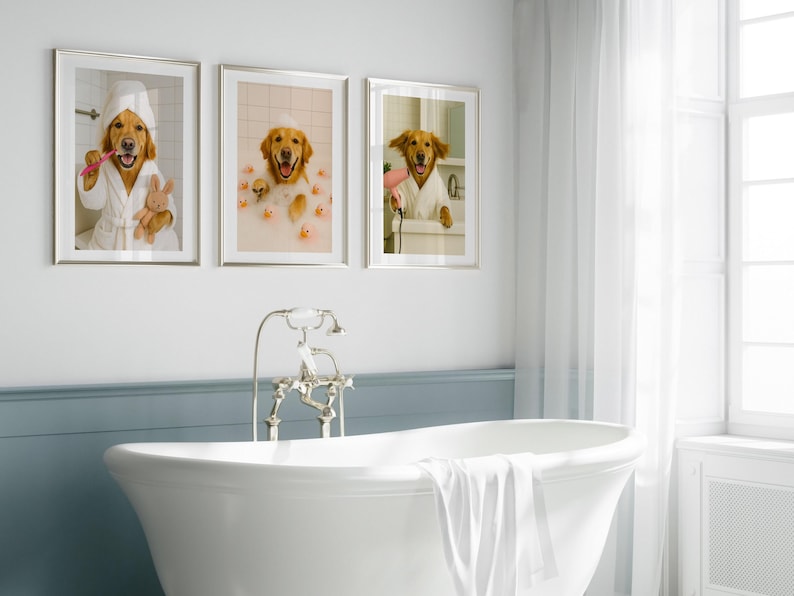 May include: Three framed prints featuring a golden retriever in a bathroom setting. One print shows the dog brushing its teeth, another in a bubble bath with rubber ducks, and the third with a hairdryer. The prints are displayed above a white bathtub.