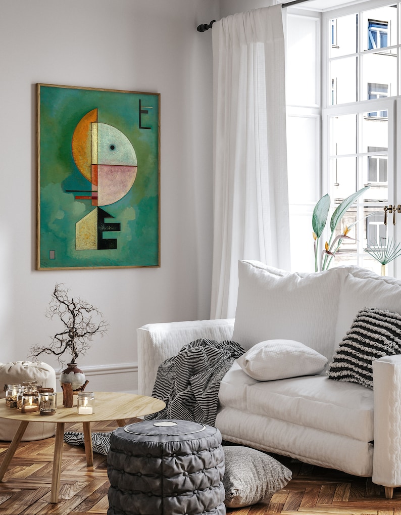 Może przedstawiać: Abstrakcyjny wydruk artystyczny w złotej ramie wisi na białej ścianie. Grafika przedstawia geometryczne kształty w kolorze pomarańczowym, r&oacute;żowym i czarnym na turkusowym tle. Pok&oacute;j obejmuje białą sofę, drewniany stolik kawowy i dekoracyjne świece.