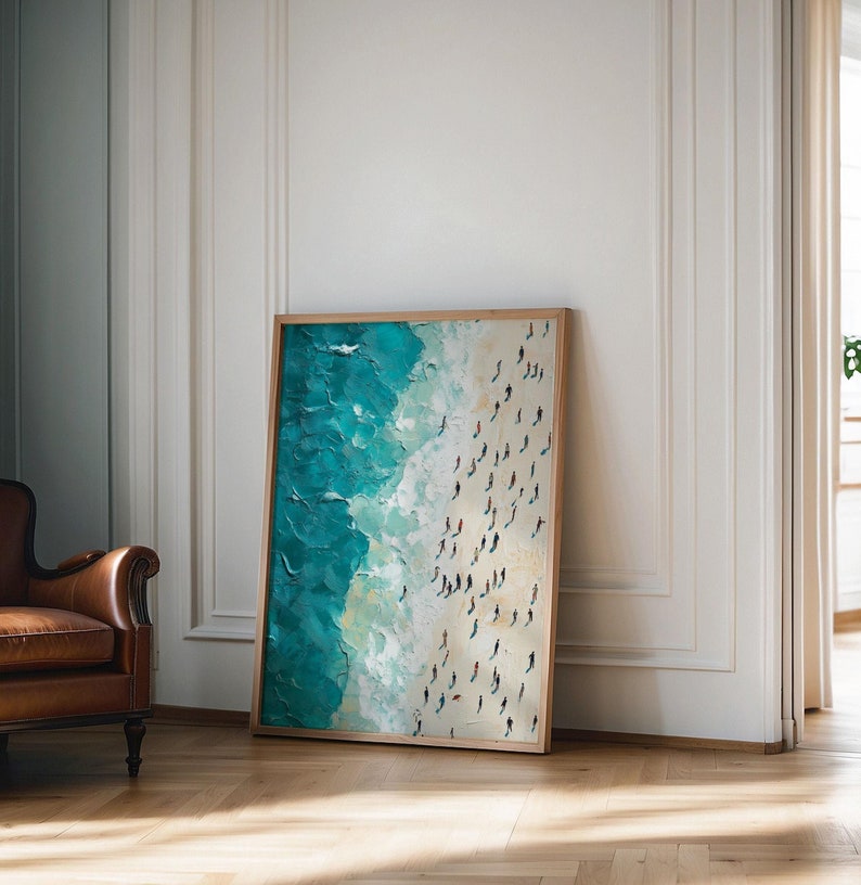 May include: A framed painting depicting a beach scene with turquoise water and white sand. The painting is viewed from above, showing a large group of people walking on the sand.
