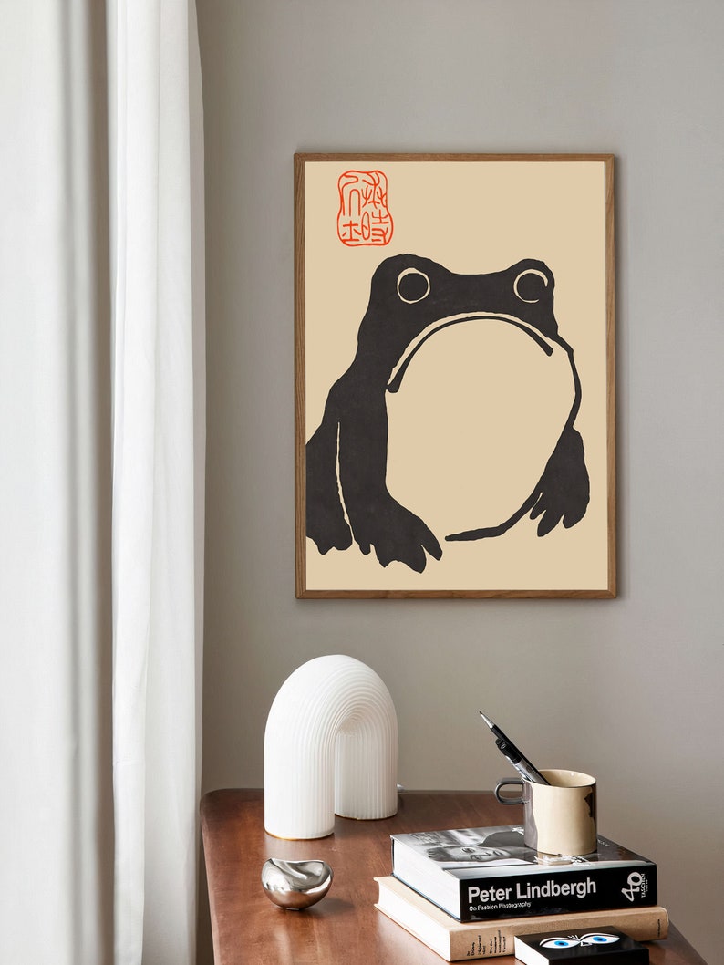 May include: A black and white illustration of a frog with a red stamp in the top left corner. The stamp has Japanese characters on it. The illustration is on a beige background.