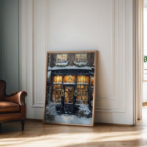 May include: A framed illustration of a storefront with a black door and windows, decorated with greenery and lights. Snow is falling in front of the store, which is lit up inside. The storefront is a bookstore with books visible in the windows.