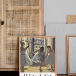 May include: A framed print of a painting by Edgar Degas titled "Three Dancers in an Exercise Hall". The painting depicts three ballerinas in white tutus practicing in a dance studio. The print is in a light wood frame.