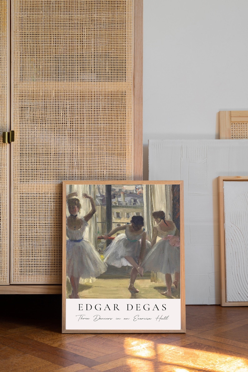 May include: A framed print of a painting by Edgar Degas titled "Three Dancers in an Exercise Hall". The painting depicts three ballerinas in white tutus practicing in a dance studio. The print is in a light wood frame.