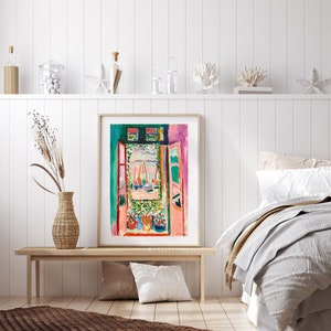 May include: A framed print of a painting depicting an open window with a view of a harbor scene. The painting is in a colorful style with shades of pink, green, blue, and yellow. The window is framed in red and the scene outside the window includes boats and a blue sky.