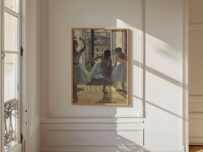 May include: A framed print of a painting by Edgar Degas featuring three ballerinas in white tutus. The painting is set in a dance studio with a window in the background. The text "DEGAS" is printed in white at the bottom of the print.