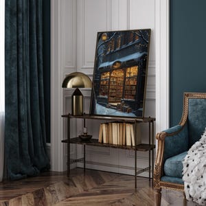 May include: A framed print of a bookstore with a snowy street scene. The bookstore is lit up with warm yellow lights and has a sign that reads "The Book Nook".