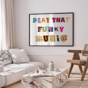 Puede incluir: Una impresi&oacute;n enmarcada con el texto "PLAY THAT FUNKY MUSIC" en letras de colores recortadas. La impresi&oacute;n est&aacute; colgada en una pared blanca sobre un sof&aacute; blanco y una silla de madera.